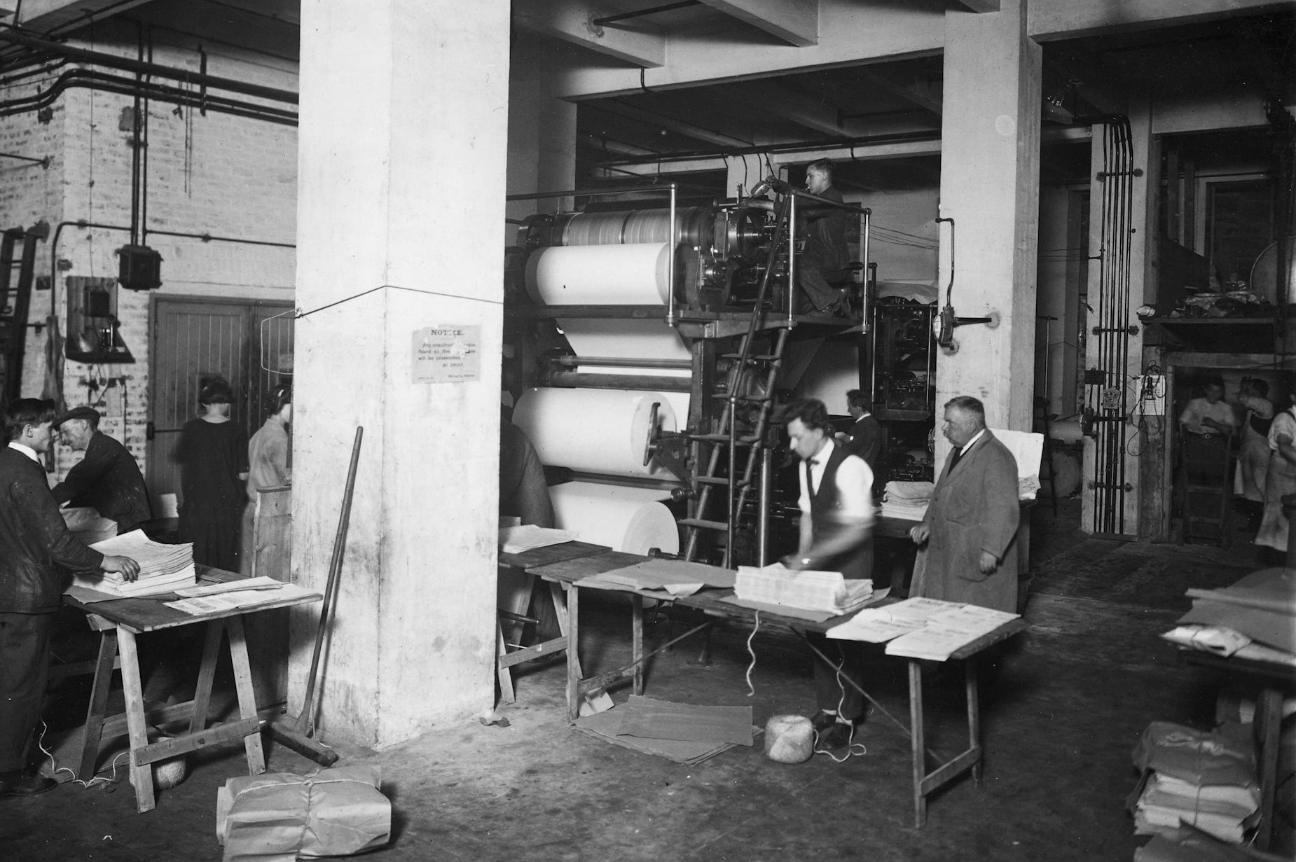 A black and white photograph of workers using printmaking machines to make newspapers in the 1930s